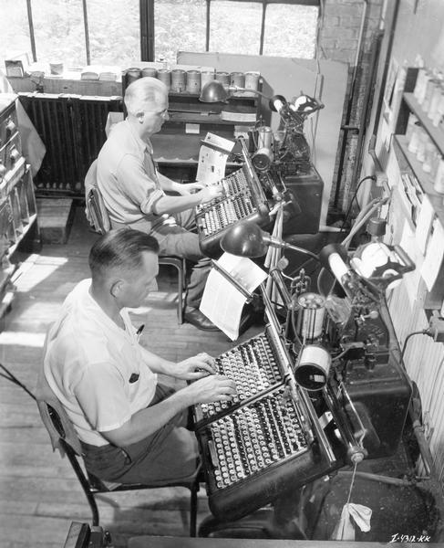 Two men operating monotype keyboards at International Harvester Press. The paper-punched product later goes through a caster, which makes new type to print from.