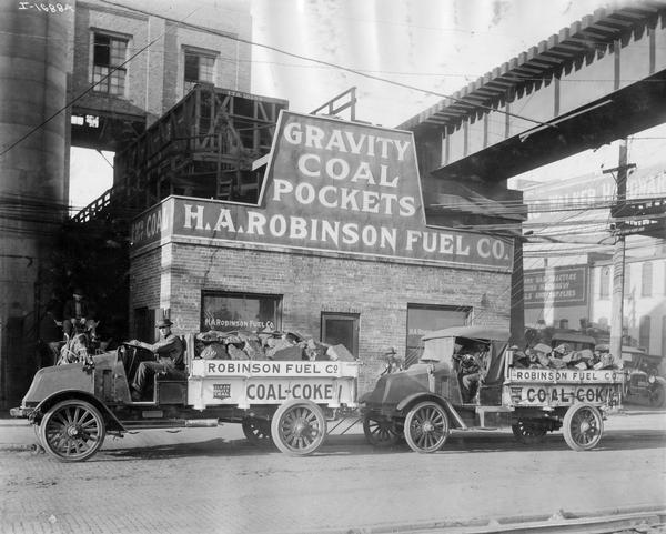 Two International two ton model G trucks hauling coal for the H.A. Robinson Fuel Co. A sign above the company's office building reads "gravity coal pockets."