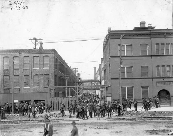 Workers milling around the factory gates at the Fullerton Avenue side of International Harvester's Deering Works. The factory was originally built by William Deering for the Deering Harvester Company in 1880. In 1902 it became International Harvester's Deering Works. The factory was located at Fullerton and Clybourn Avenues and closed in 1933.