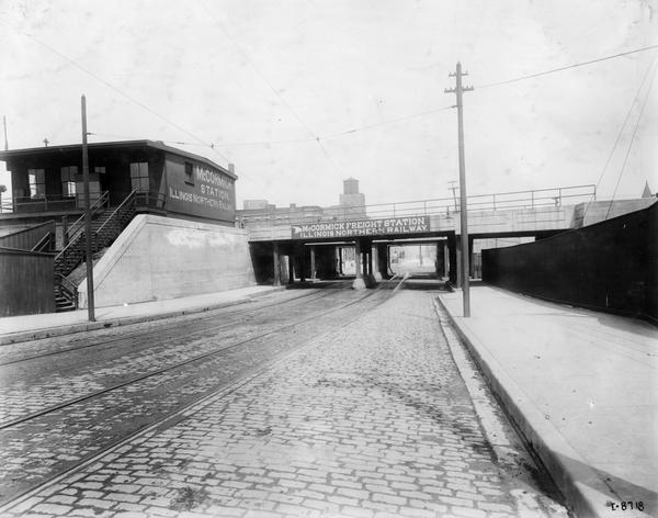 An empty street outside McCormick Station on the Illinois Northern Railway. An overpass bears a sign for the McCormick Freight Station on the same railroad line.