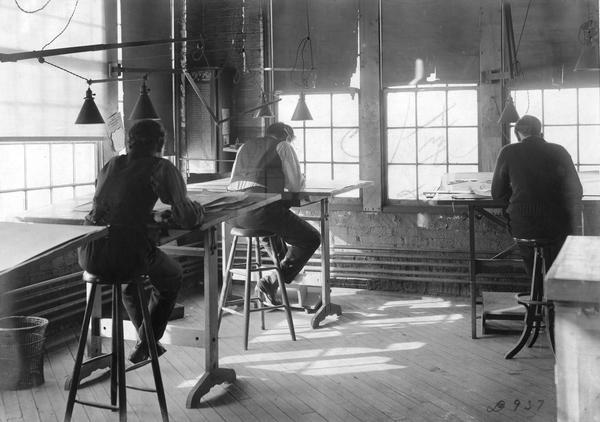 Three draftsmen are working at their desks at International Harvester's Deering Works. The factory was originally built by William Deering for the Deering Harvester Company in 1880. In 1902 it became International Harvester's Deering Works. The factory was located at Fullerton and Clybourn Avenues and closed in 1933.