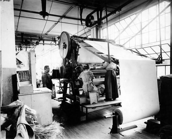 A man and two women working in the canvas department at International Harvester's Deering Works (factory). The canvas was likely used for grain binders, harvester-threshers (combines) and push machines. The Deering Works was built by William Deering for the Deering Harvester Company in 1880. In 1902 the factory became International Harvester's Deering Works. It was located at Fullerton and Clybourn Avenues and closed in 1933.