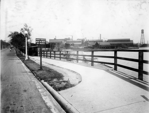 Deering Works factory seen across the waterfront from Diversey Avenue. In the foreground is a street and sidewalk with the sign "horse vehicles keep to right of road." The factory was originally built by William Deering for the Deering Harvester Company in 1880. In 1902 it became International Harvester's Deering Works. The factory was located at Fullerton and Clybourn Avenues and closed in 1933.