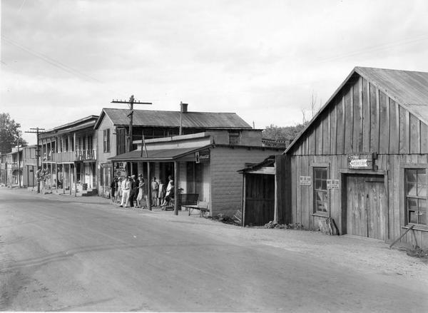 People assembled at storefront along the street of a small town in "poor farming country."
