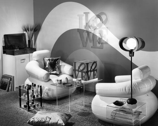 "Modern" 1970s style room with "love" design, white vinyl chairs, flowered coffee mugs and Plexiglas furnishings. Includes a stack of records with "The In Crowd" by the Ramsey Lewis Trio on top.