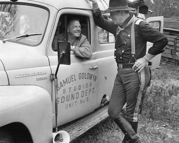 Actor John Wayne chats with driver Jim De Shon in an International Travelall sound truck on the set of "The Horse Soldiers". Owned by Goldwyn Studios and housing a five-man crew, the truck helped turn the woods and fields of a Mississippi plantation into a soundstage for director John Ford's movie.