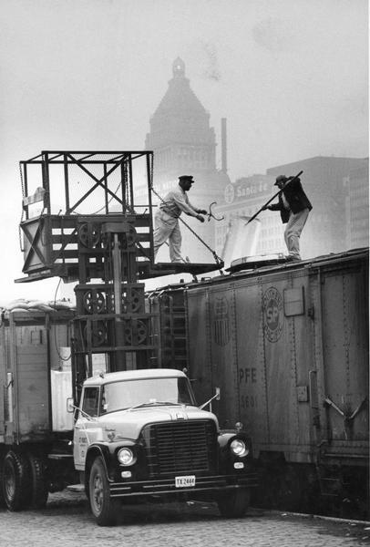 Two workers filling a railroad cooling car with ice from an International truck at a railroad yard.