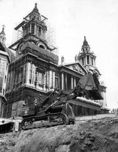 A man excavating with a British built International BTD-6 crawler tractor and Drott bucketloader in front of the west facade of St. Paul's Cathedral in London.