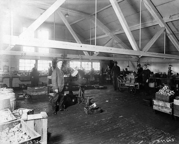 Workers in a shop inside International Harvester's Akron Works. Bins containing metal parts and tools are scattered around the floor. The factory was devoted primarily to the manufacture of trucks. The works originally belonged to the Aultman & Miller Buckeye Company until it was bought out by IHC in 1905. Retooled and modernized in 1907, the works unfortunately burned and was rebuilt in 1912. Occupying 11.5 land acres, the works closed in 1919 when truck manufacturing was moved to Springfield Works. Products manufactured: harvesters (Buckeyes, until 1906 or so), auto wagons, commercial cars, motor truck parts, tractors (until 1911).