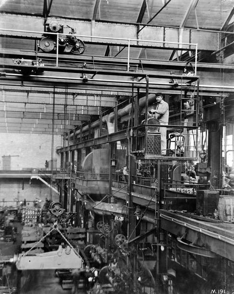 A worker lifting a stationary gas engine frame with an overhead crane at International Harvester's Milwaukee Works. The factory was owned by the Milwaukee Harvester Company until 1902.