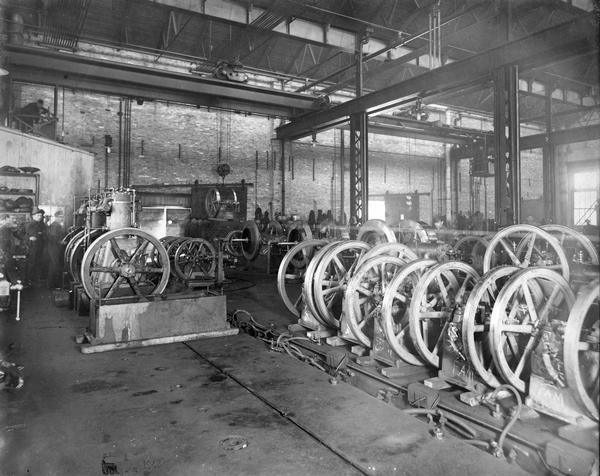 Men working on stationary engines at International Harvester's Milwaukee Works. Some of the engines are marked with the letters "FAM" which may refer to the "Famous" brand name. The factory was owned by the Milwaukee Harvester Company until 1902.