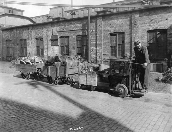 Worker using a motorized shop cart ("shop mule") to transport parts between buildings at International Harvester's Milwaukee Works. The cart was manufactured by the Automatic Transportation Company of Buffalo, New York. The Milwaukee Works factory was owned by the Milwaukee Harvester Company until 1902.