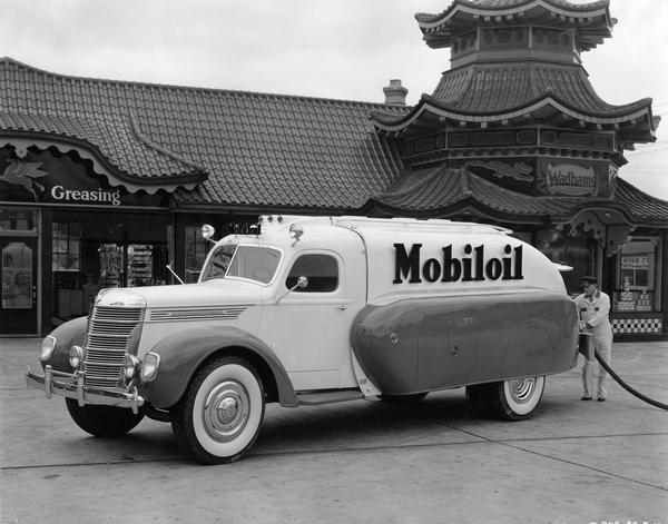 Service station attendant pumping gas from an International DR-60 Mobiloil fuel truck at a Wadham's Oil and Grease Company station. Centered in Milwaukee, Wisconsin, the Wadham's chain featured distinctive pagoda-like buildings. The truck, which has a 179" wheelbase, has a FBB 401 engine and a 1600 gallon capacity fuel tank.