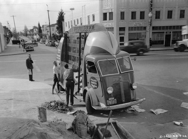 Two men unloading a pane of glass from an International C-300 truck with special streamlined body designed for transporting large panes of plate glass without lifting over the rear wheels. The glass was for a Firestone auto supply and service station under construction. The truck was owned by W.P. Fuller & Co. The wheelbase of the truck was extended to 184.5 inches so as to allow for a carrying rack approximately 11 feet long, 8 feet high, and 14 inched deep on each side of the truck. The rear six feet of space within the body was fitted with cushioned seats for workmen. The over-all length was 24 feet, with a height of 10.5 feet.