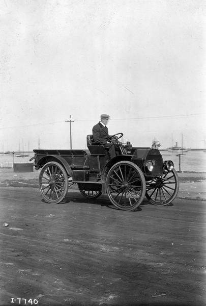 Man driving an International Model M highwheeler with the Chicago skyline in the background. The Model M, introduced in 1915, was rated at 1000 pounds carrying capacity and featured a heavy-duty water cooled engine.