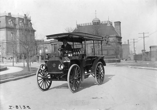 Man driving an International Model M highwheeler with roof. The Model M, introduced in 1915, was rated at 1000 pounds carrying capacity and featured a heavy-duty water cooled engine.