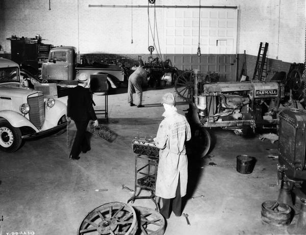 Elevated view of men at work on an engine block inside the service shop of a McCormick-Deering dealership owned by C. Scheler and Son. In background are International trucks and a Farmall tractor.