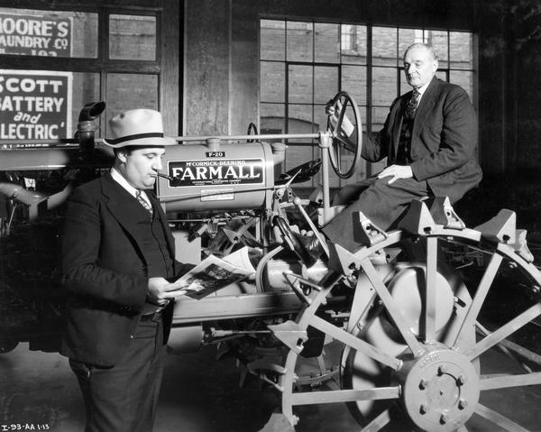 Two salesmen (C. Scheler and son?) posing with a new Farmall F-20 tractor inside the dealership of C. Scheler and Son.