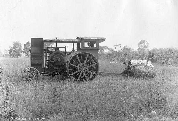 Two men operating a Mogul 15-30(?) tractor and a McCormick binder in a field.