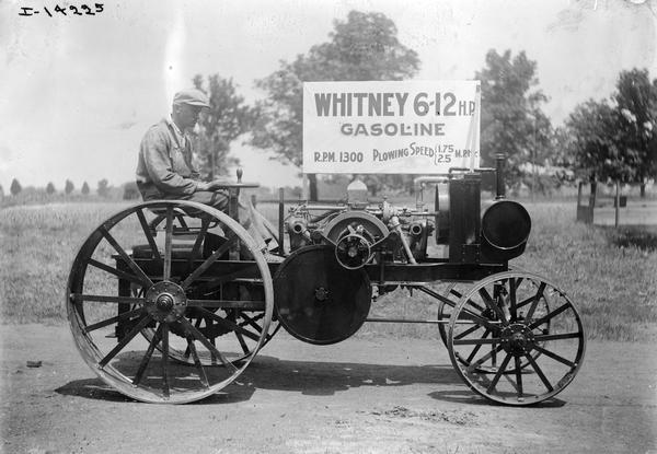Man riding a Whitney 6-12 light-weight gasoline tractor. Placard reads "r.p.m. 1300, plowing speed 1.75-2.5 m.p.h." The tractor was sold in small numbers by International Harvester and by Whitney.