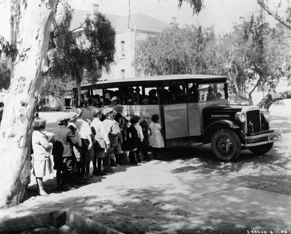 Group of school children boarding a crowded International Model 52 or 53 motor coach school bus.