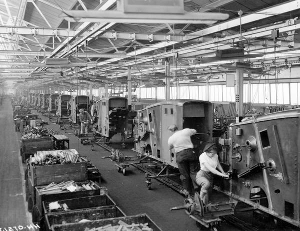 Male and female workers installing parts on combine bodies along assembly line at International Harvester's East Moline Works. The factory was constructed in 1933 and was located at 1100 3rd Street.