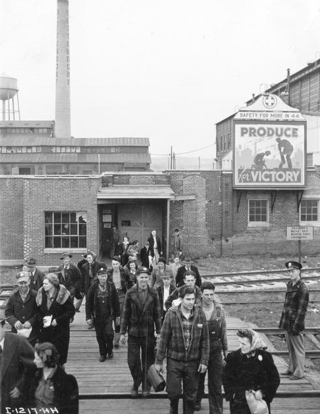 Employees leaving International Harvester's Bettendorf Works at the end of their work day. A sign in the background reads "Produce for Victory."