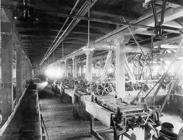 Workers operating machines for separating fibre (fiber) from straw inside the St. Paul Flax and Twine Mill. The factory was owned and operated by the International Flax Twine Company (originally Minnie Harvester Company), a subsidiary of International Harvester. The factory produced binder twine.