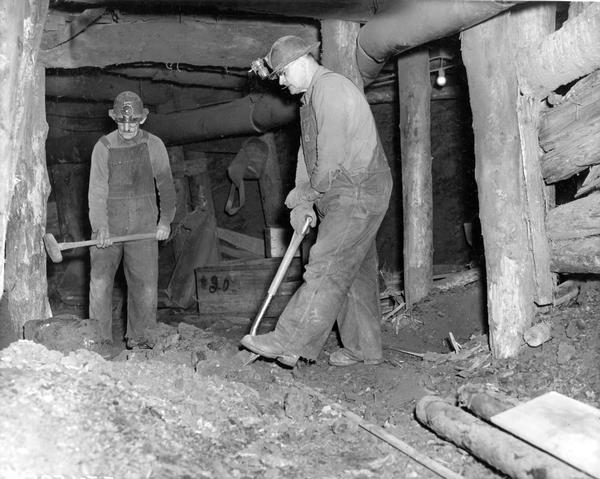 Two miners at work with shovel and hammer inside International Harvester's Hawkins Mine.