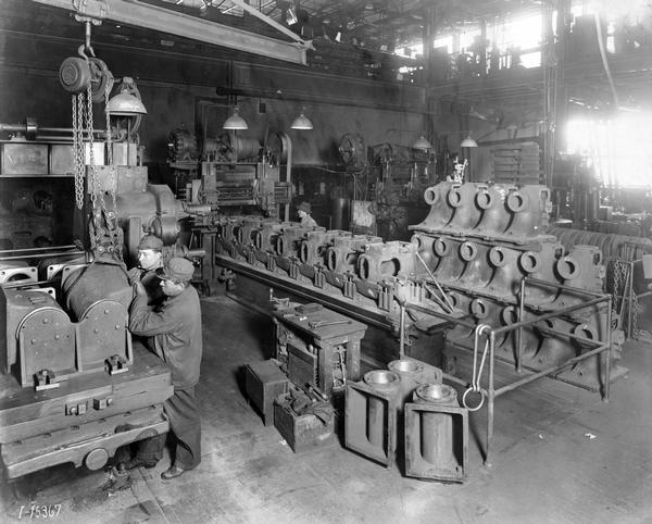 Factory workers using a pulley to load castings onto a table at International Harvester's Tractor Works. The factory produced tractors (including Farmall A and B from 1939-1947), construction equipment, and crawler tractors.