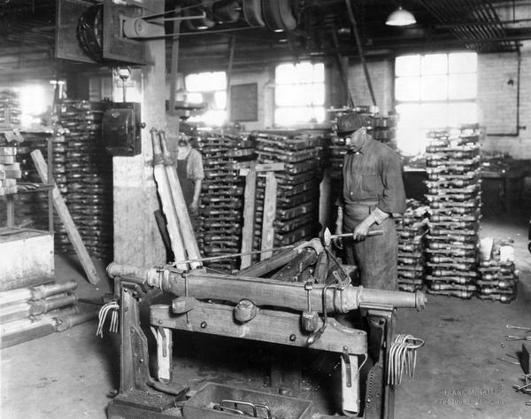African American worker assembling a wagon axle running gear while a co-worker is looking on at International Harvester's Weber Wagon Works. The factory was located at Auburn Park and was owned by the Weber Wagon Company until 1904. International Harvester produced wagons at the factory until 1927.