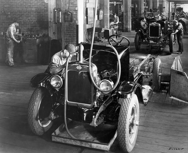 Assembly line worker inspecting a truck's engine compartment during testing operations at International Harvester's Chatham Works. The factory was owned by the Chatham Manufacturing Company before 1920.