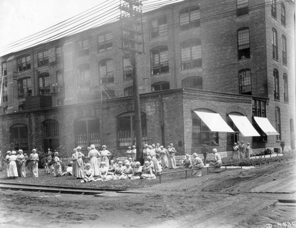 Women sitting and standing at leisure outside International Harvester's Deering Works twine mill. The factory was owned by the Deering Harvester Company until 1902, when it became part of International Harvester Company.