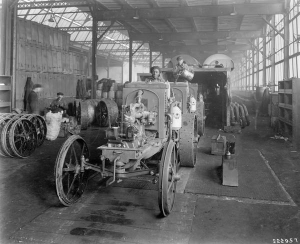 An African American worker driving a partially assembled International 8-16 tractor on an assembly line at International Harvester's Tractor Works. Another worker is adding fuel to a tractor in the background. Tractor Works was in operation from 1910 to 1972 and was located at 2600 West 31st Blvd.