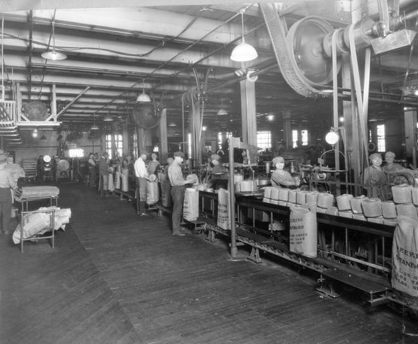 Male and female workers producing balls of twine and placing them in burlap bags. The McCormick Works was built by Cyrus McCormick in 1873 and became part of International Harvester in 1902. The factory was located at Blue Island and Western Avenues in the Chicago subdivision called "Canalport." It was closed in 1961.