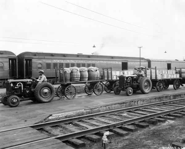 Two African American workers use McCormick-Deering I-12 industrial tractors with attached wagons to haul cargo at a Jacksonville rail station.  The men worked for Southeastern Express Company. A passenger coach in the background bears the name "Atlantic Coast Line."