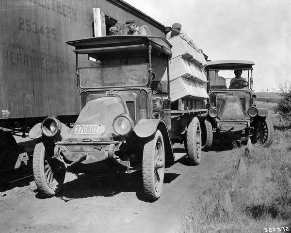 Three men loading wooden crates from the back of an International Model F or 31 truck into a refrigerated railroad car.