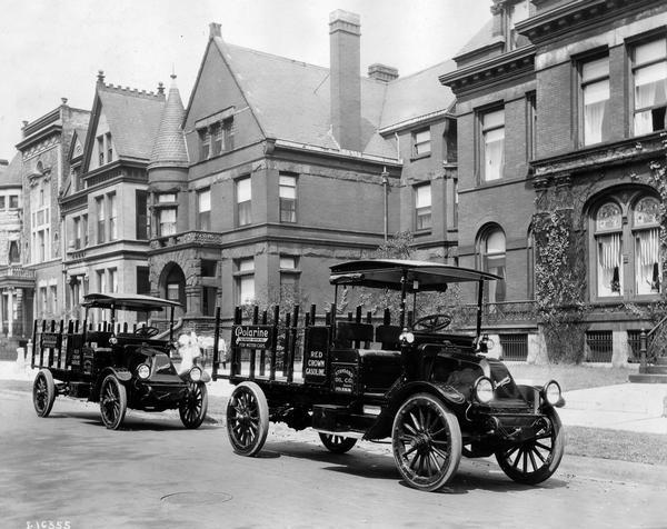 Two International 1 1/2 ton Model F trucks parked along an urban residential street. The trucks were owned and operated by Standard Oil Company and carried  advertisements for "Polarine" motor oil and "Red Crown" gasoline.