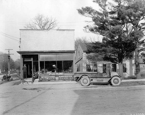 International Model H or 21 truck, farm equipment, and two employees in front of the Butler and Peckels International Harvester dealership. Signs in the window advertise McCormick-Deering farm equipment and P&O plows.