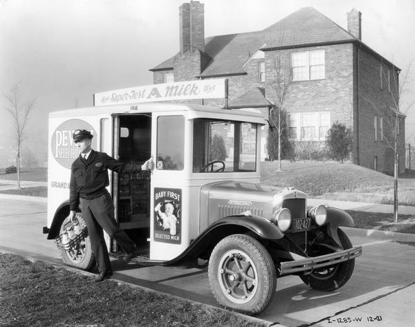 Milkman delivering bottles of milk and other dairy products to a residential home from an International Model M-2 milk truck. The truck was owned by Pevely Selected Milk Co. An advertisement for "Baby First Selected Milk" is on side of the truck. The M-2 was designed exclusively as a milk delivery vehicle. It had a 118 inch wheelbase, 186 cubic inch four cylinder engine, Warner T-9 transmission, and IHC rear axle. The body was built with a special treatment of its wood components to resist lactic acid damage.
