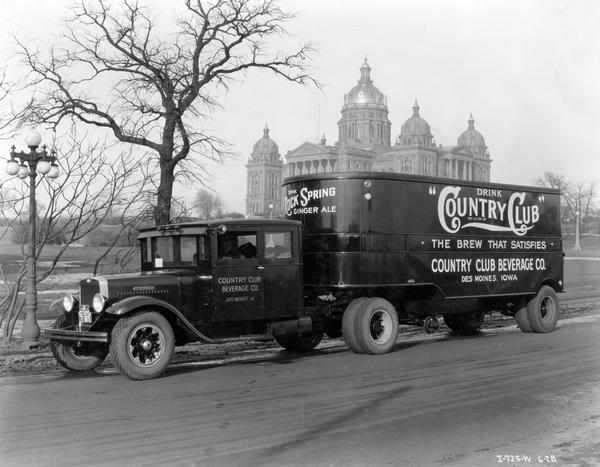 International Model A-4 semi-tractor with sleeper cab and trailer parked in foreground, with the Iowa State Capitol Building in the background. The truck was owned and operated by Country Club Beverage Company. The trailer carries an advertisement for Country Club ginger ale.