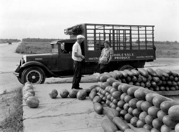 Merchant Charles Jankowski and a customer standing among stacks of watermelons at a roadside produce stand. Mr. Jankowki's International Model A-4 truck is in the background.