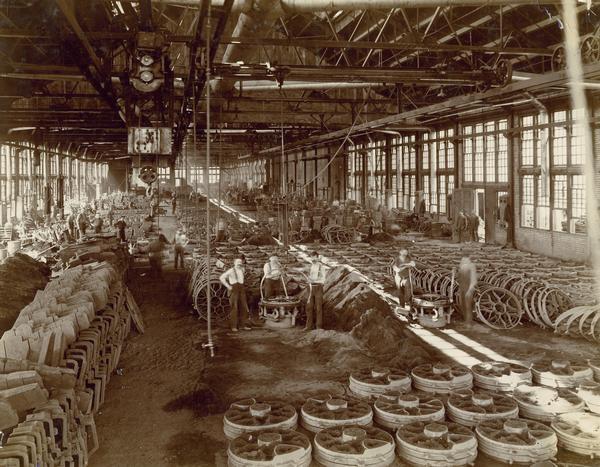 Workers in the grey iron foundry at International Harvester's Hamilton Works. In the foreground workers are removing implement wheels from casting molds.