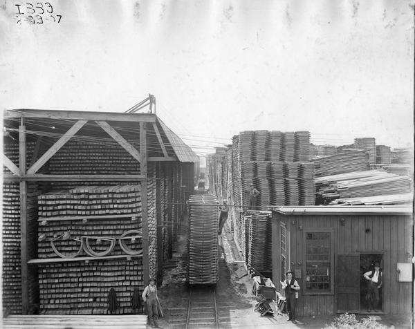 Elevated view of workers with a rail cart full of stock lumber in the lumberyard at International Harvester's Weber Works in Auburn Park. The factory was owned by the Weber Wagon Company until 1904 when it was purchased by International Harvester. The photograph bears a stamp that reads: "Used at 1915 Expositions."