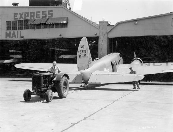 Two workmen use a McCormick-Deering I-12 industrial tractor to a pull Boeing U.S. mail and express airplane from a Municipal Airport hangar during the American Air Races, July 1-5.