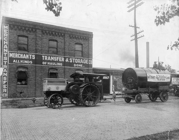 International Titan 45 tractor pulling a 42,000 pound load on an attached wagon car in front of a warehouse owned by Merchants Transfer and Storage. The Titan 45 had a open cooling system, while the Titian 30-60 had a closed cooling system.