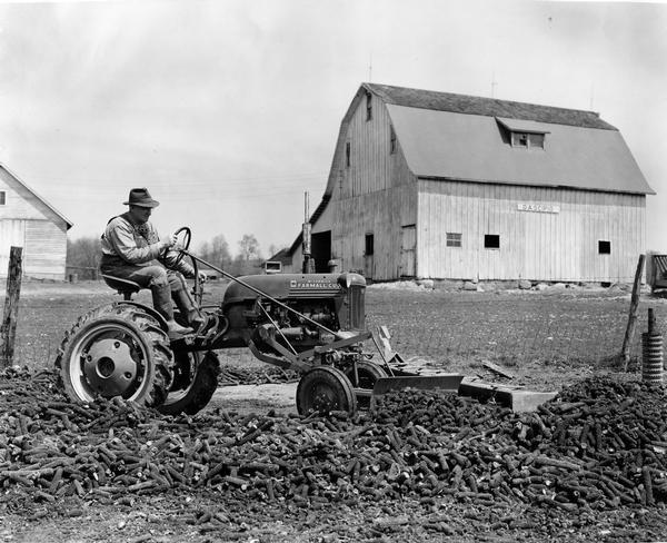Farmer O.A. Scipio cleaning the concrete hog feeding floor on his farm with a McCormick Farmall Cub tractor and attached leveling and grading blade.