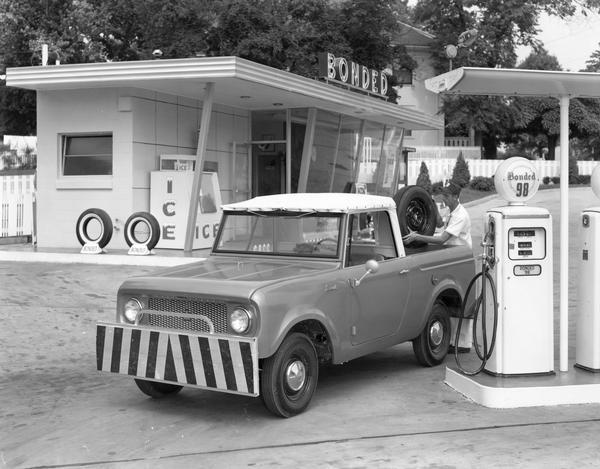 Bonded service station attendant loading a tire into the back of a 1961 International Scout convertible pickup owned by the station.