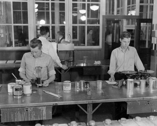 Workers testing paint for physical constancy, viscosity and weight per gallon in the Paint Department of International Harvester's McCormick Works. Cans of "International Harvester Farm Machine Varnish Enamel Paint" and "International Harvester Motor Truck and Tractor Synthetic Enamel Paint" are on the work table. The McCormick Works was built by Cyrus McCormick in 1873 and became part of International Harvester in 1902. The factory was located at Blue Island and Western Avenues in the Chicago subdivision called "Canalport." It was closed in 1961.