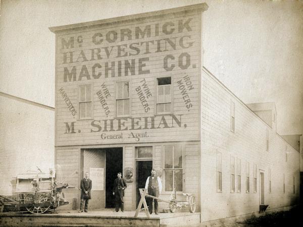 Three men posing with a McCormick mower and binder in front of M. Sheehan's McCormick Harvesting Machine Company dealership. A note on the back of the print reads: "Fargo, D.T. [Dakota Territory]."